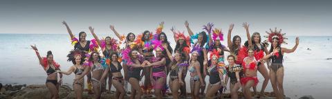 This image shows a group of people on a beach wearing colorful costumes adorned with feathers