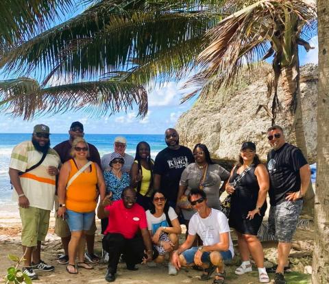 The image features a group of twelve people posing for a photograph on a beach