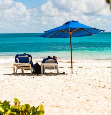 This image shows a serene beach scene with two lounge chairs shaded under a blue umbrella