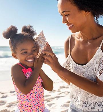This image shows a joyful moment between a woman and a young girl on a sunny beach