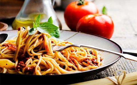 The image displays a plate of spaghetti with tomato-based sauce garnished with fresh basil leaves