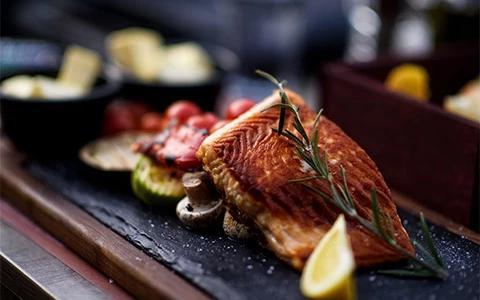 The image features a beautifully presented dish of grilled salmon fillet served on a wooden board