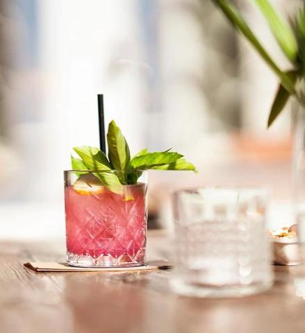 The image shows a refreshing beverage in a textured glass, adorned with a garnish of fresh basil leaves and a slice of lemon