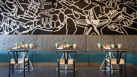 This image shows a stylish indoor dining area, featuring a large black and white abstract mural on the wall