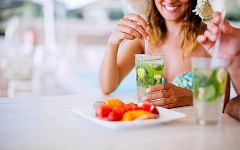 The image shows a person at a table, holding a glass with a refreshing drink, possibly a mojito, containing slices of lime and mint leaves