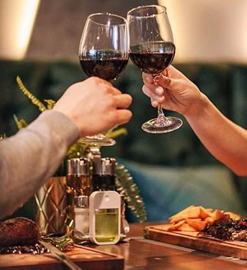 The image shows two people toasting with red wine glasses