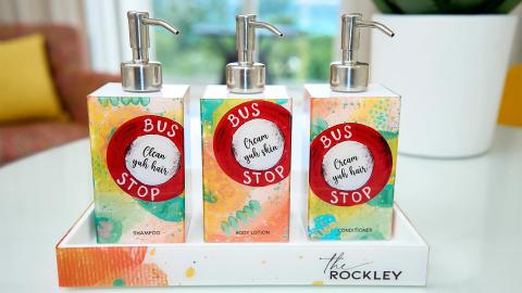 The image shows a set of three colorful toiletry dispensers arranged neatly in a tray