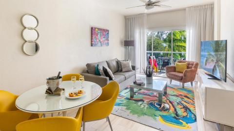 This image shows a stylishly decorated living room that leads onto a balcony with a lovely view of tropical foliage