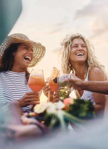The image captures two joyful women outdoors, possibly enjoying a sunset or a pleasant summer evening