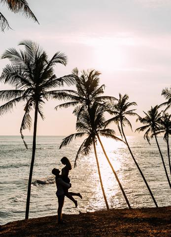 This image captures a romantic and scenic moment with a couple by the sea at sunset