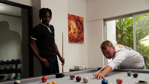 This image depicts two men playing a game of pool in a bright, stylishly decorated room