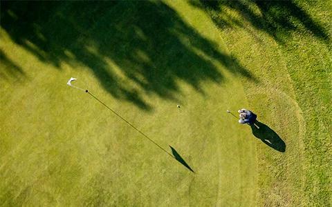 This image captures a scene from an aerial perspective of a golf course, showing a lush green surface with well-maintained grass