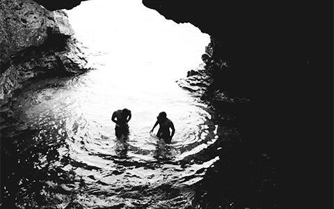 This image shows two people in a body of water, likely a natural pool or a cave with an opening above that allows light to enter